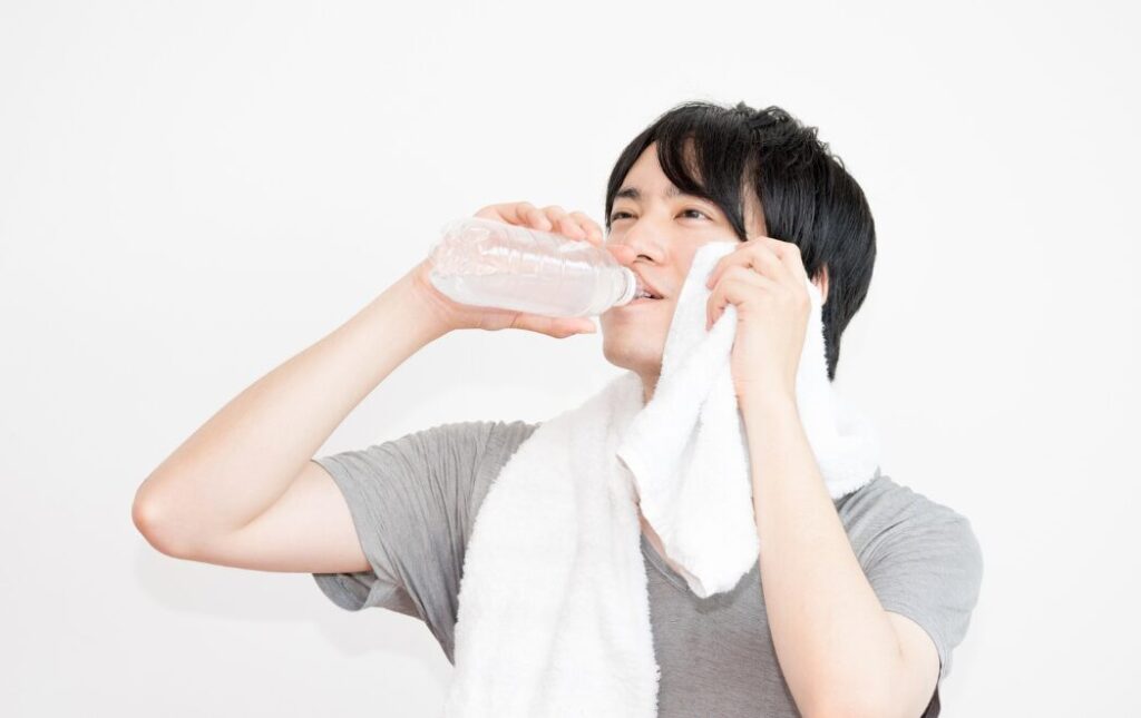 汗を拭きながらスポーツドリンクを飲む男性