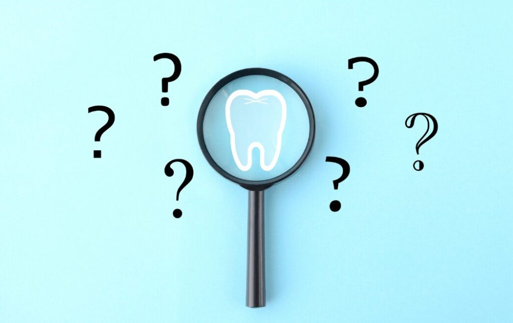 虫眼鏡の中い歯のイラスト、外にクエスチョンマークが6個浮かんでいる